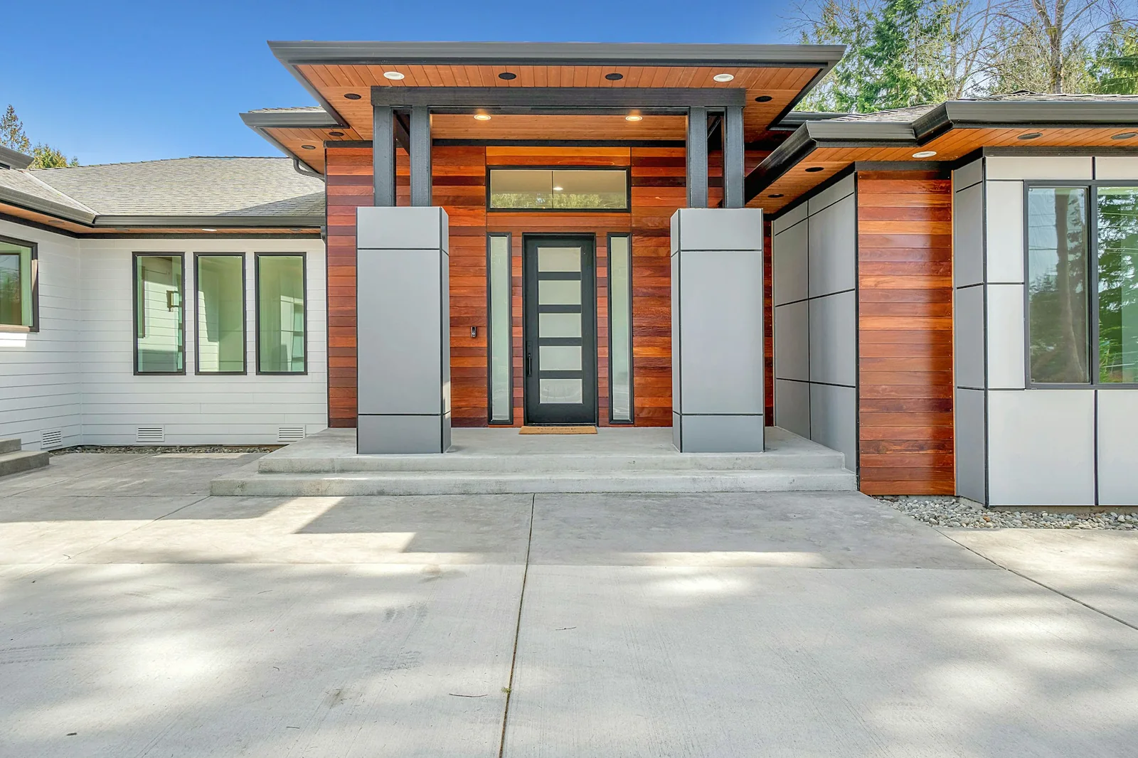 Charcoal entrance door with frosted glass and sidelights, surrounded by warm timber and grey cladding